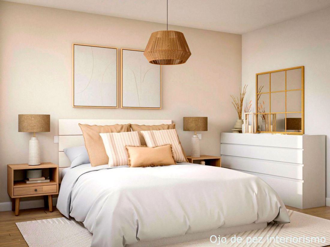 Dormitorio con muebles y edredón en blanco y cojines, lámparas y cuadros en tono ocre